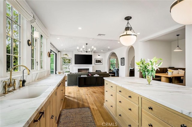 kitchen with light brown cabinetry, sink, light stone counters, decorative light fixtures, and light hardwood / wood-style floors