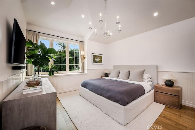 bedroom with an inviting chandelier, lofted ceiling, and light wood-type flooring