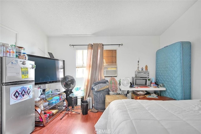 bedroom with hardwood / wood-style floors, stainless steel refrigerator, and a textured ceiling