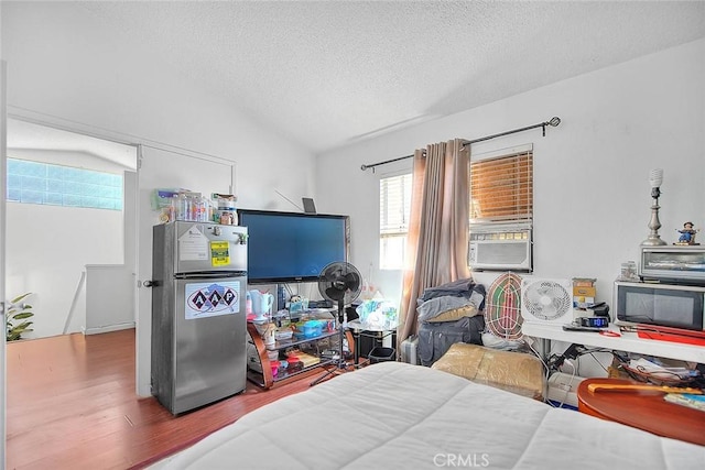 bedroom with vaulted ceiling, wood-type flooring, cooling unit, stainless steel fridge, and a textured ceiling