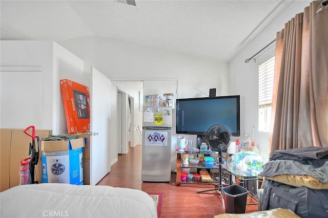 bedroom featuring lofted ceiling, hardwood / wood-style floors, stainless steel fridge, and a textured ceiling