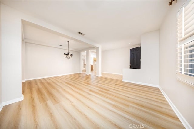 unfurnished living room featuring an inviting chandelier and light hardwood / wood-style flooring