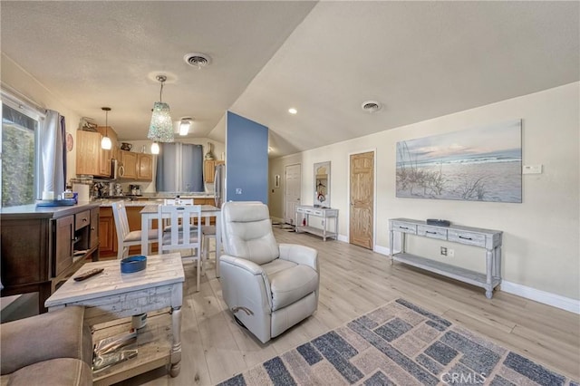 living area with light wood-style floors, visible vents, and vaulted ceiling