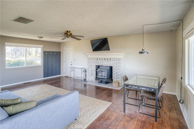 living room with dark hardwood / wood-style flooring, a textured ceiling, ceiling fan, and a wood stove