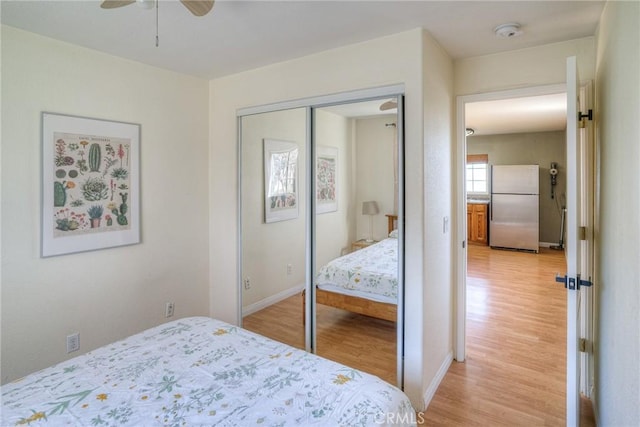 bedroom with a closet, light hardwood / wood-style flooring, stainless steel refrigerator, and ceiling fan