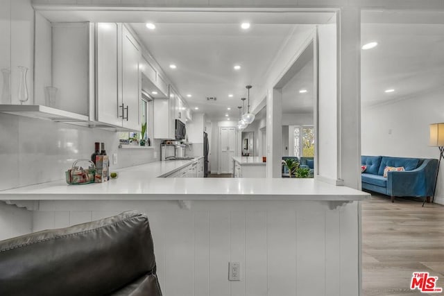 kitchen featuring a breakfast bar, white cabinetry, hanging light fixtures, light hardwood / wood-style floors, and kitchen peninsula