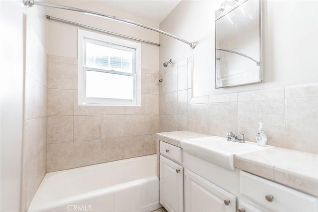 bathroom featuring tiled shower / bath combo, vanity, and tile walls