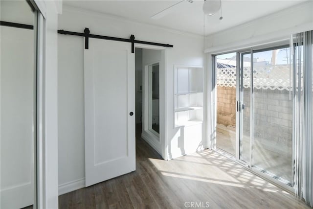 interior space featuring crown molding, access to outside, dark hardwood / wood-style floors, ceiling fan, and a barn door