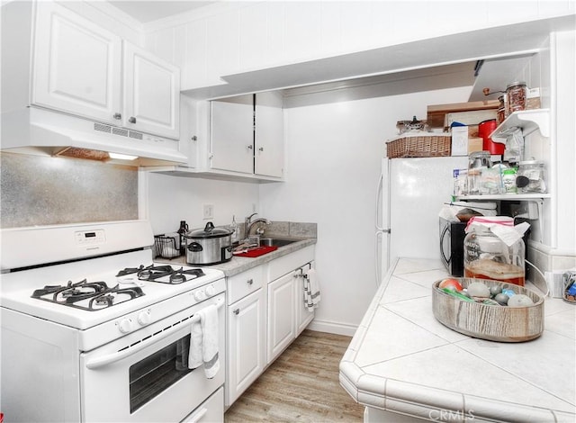 kitchen with white cabinetry, sink, light wood-type flooring, tile counters, and white appliances