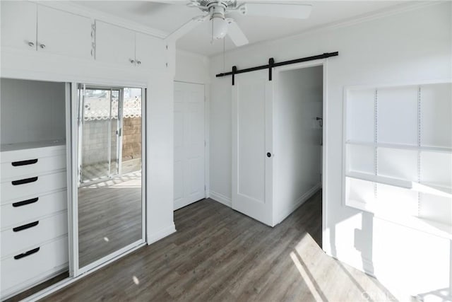 unfurnished bedroom featuring ornamental molding, a barn door, dark hardwood / wood-style floors, and ceiling fan