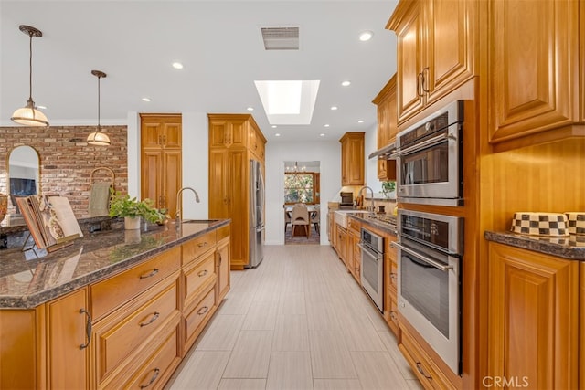 kitchen featuring sink, a skylight, dark stone countertops, pendant lighting, and stainless steel appliances