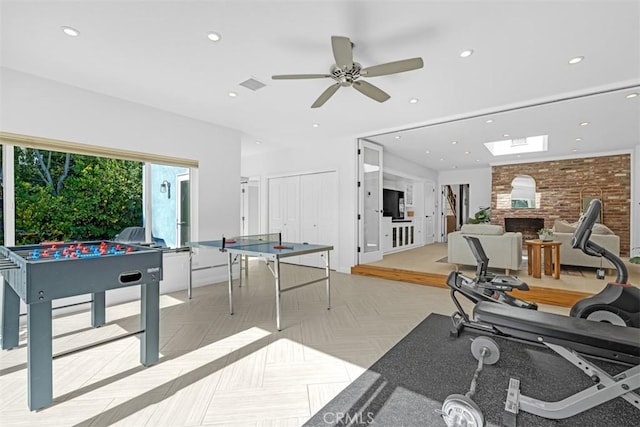 recreation room featuring ceiling fan, a large fireplace, light parquet flooring, and brick wall