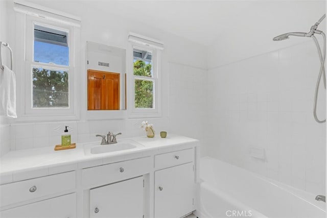 bathroom featuring vanity, tiled shower / bath combo, and backsplash