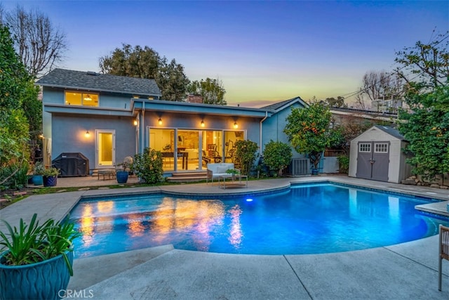 pool at dusk featuring a patio, area for grilling, central air condition unit, and a storage shed