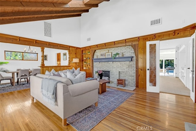 living room with wood ceiling, beamed ceiling, light hardwood / wood-style floors, a brick fireplace, and a chandelier