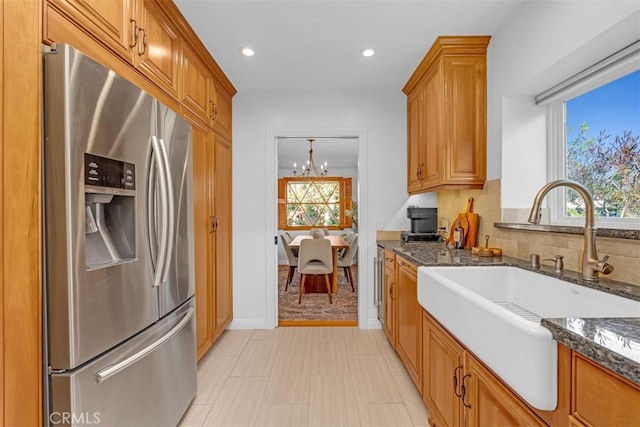 kitchen with stainless steel refrigerator with ice dispenser, sink, an inviting chandelier, dark stone counters, and decorative backsplash