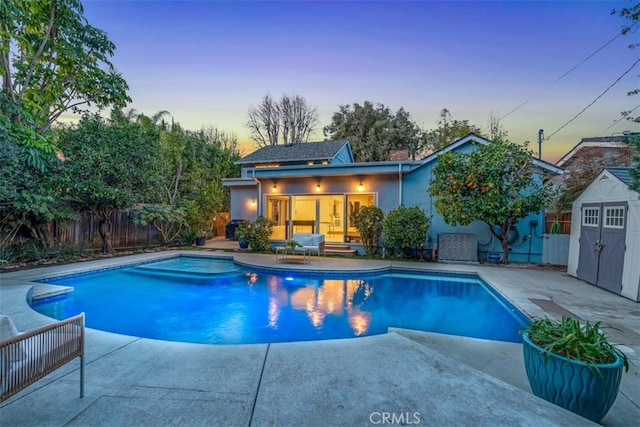 pool at dusk featuring a storage shed and a patio