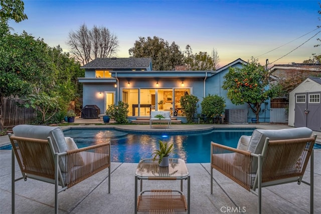 pool at dusk featuring area for grilling, a shed, and a patio