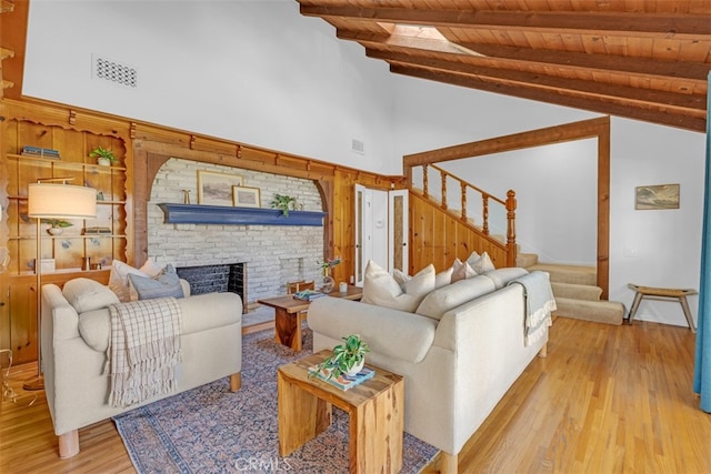 living room featuring beam ceiling, high vaulted ceiling, a fireplace, light hardwood / wood-style floors, and wooden ceiling