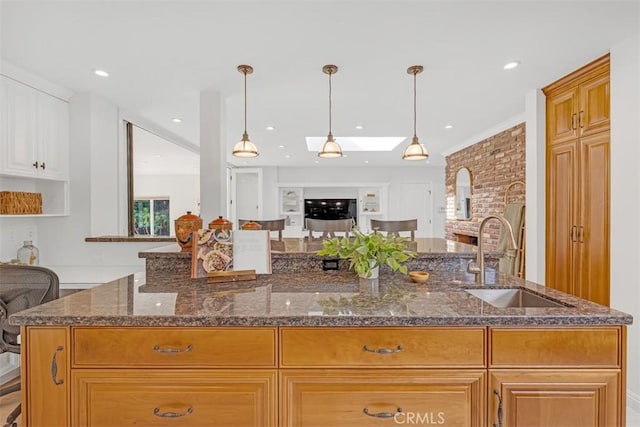 kitchen featuring sink, hanging light fixtures, dark stone counters, and a center island with sink