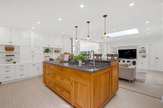 kitchen with sink, hanging light fixtures, a skylight, an island with sink, and white cabinets