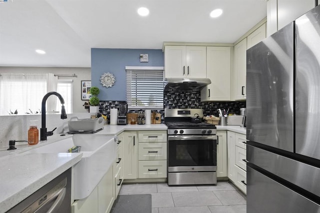 kitchen featuring light tile patterned floors, stainless steel appliances, ventilation hood, decorative backsplash, and cream cabinetry