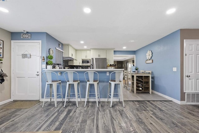 kitchen with a breakfast bar area, appliances with stainless steel finishes, kitchen peninsula, hardwood / wood-style floors, and white cabinets