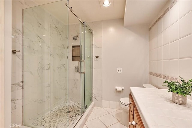 bathroom with tile walls, an enclosed shower, vanity, tile patterned floors, and toilet