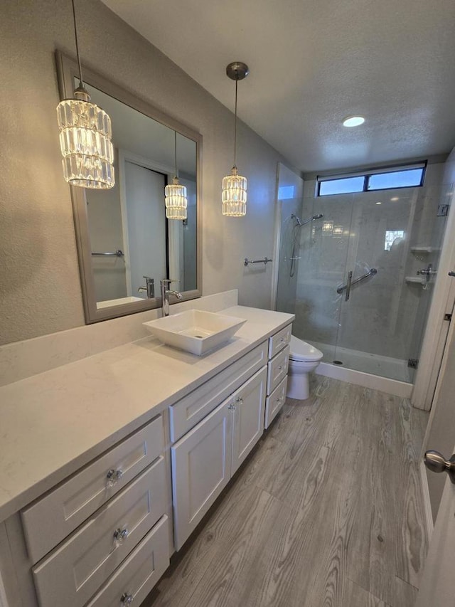 bathroom featuring a shower with door, vanity, wood-type flooring, a textured ceiling, and toilet