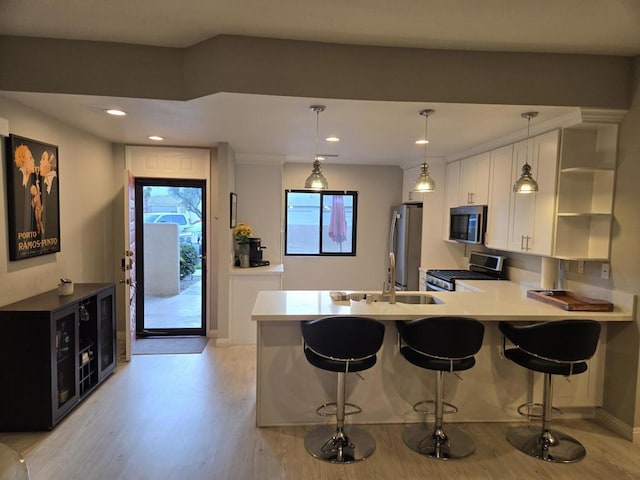 kitchen with a breakfast bar area, appliances with stainless steel finishes, kitchen peninsula, pendant lighting, and white cabinets