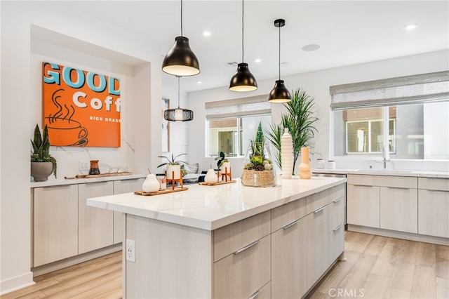 kitchen with a kitchen island, sink, hanging light fixtures, light stone countertops, and light wood-type flooring