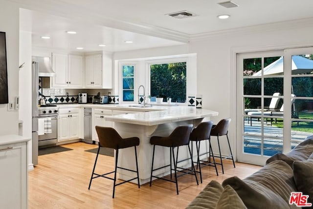 kitchen with a breakfast bar, sink, white cabinetry, kitchen peninsula, and high end stove