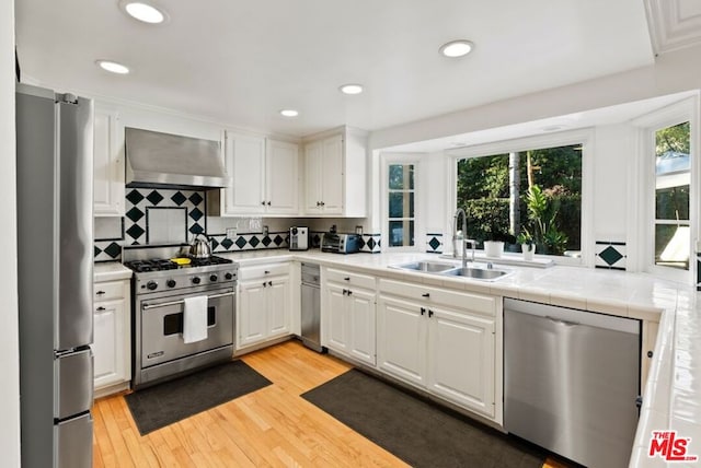 kitchen with stainless steel appliances, white cabinetry, and wall chimney exhaust hood