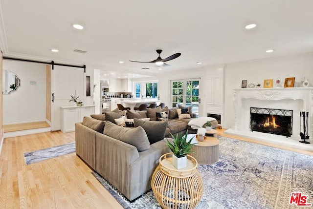 living room with crown molding, ceiling fan, a barn door, and light wood-type flooring