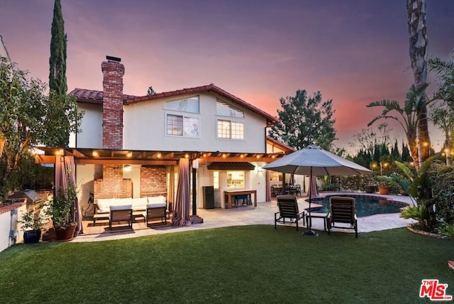 back house at dusk with outdoor lounge area, a yard, exterior bar, and a patio area