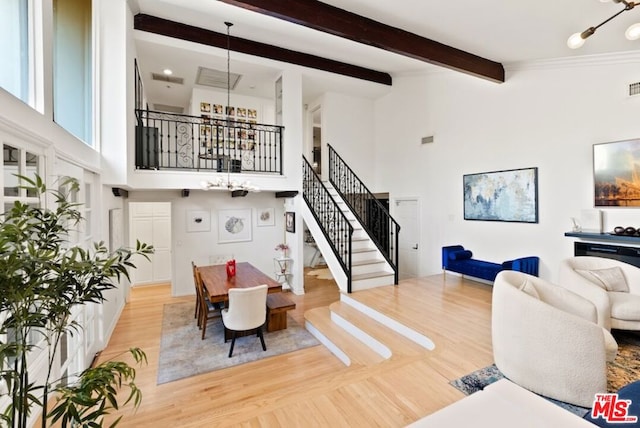 living room featuring beamed ceiling, a high ceiling, hardwood / wood-style flooring, and a notable chandelier