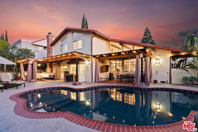 pool at dusk with a patio, an outdoor hangout area, and a pergola