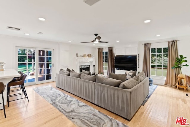 living room with ceiling fan, a fireplace, light wood-type flooring, and french doors