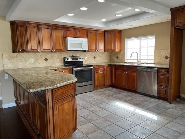 kitchen with sink, stainless steel appliances, light stone countertops, kitchen peninsula, and a raised ceiling