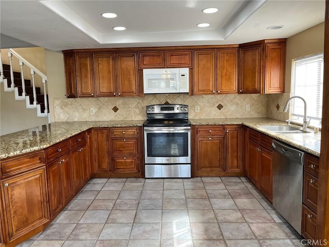 kitchen with appliances with stainless steel finishes, sink, kitchen peninsula, a raised ceiling, and light stone countertops