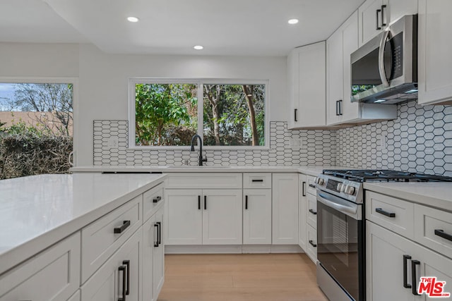 kitchen with white cabinetry, sink, backsplash, and stainless steel appliances