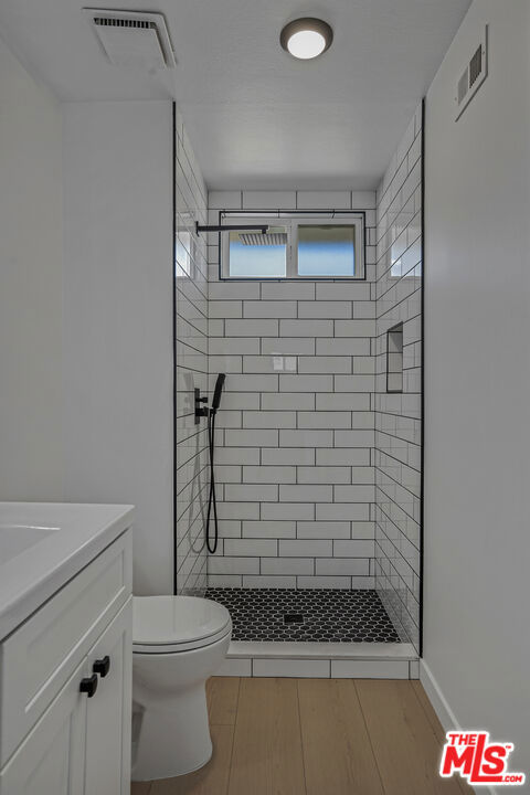 bathroom featuring hardwood / wood-style floors, vanity, a tile shower, and toilet