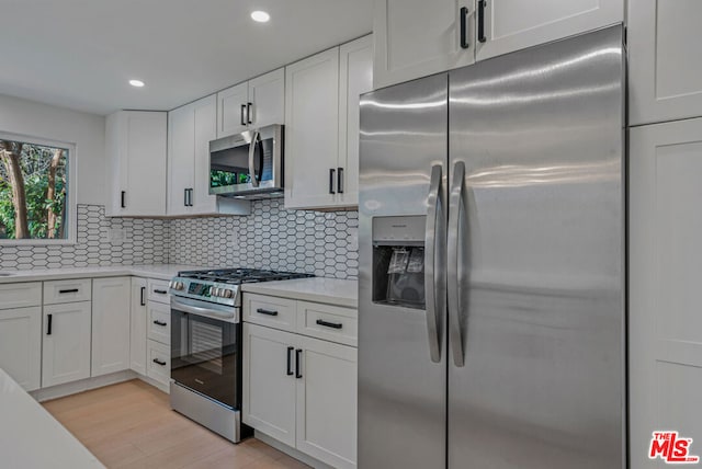 kitchen with appliances with stainless steel finishes, white cabinets, backsplash, and light hardwood / wood-style flooring