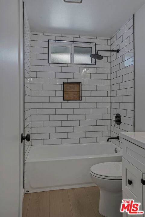 full bathroom with tiled shower / bath combo, wood-type flooring, vanity, and toilet