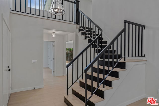 stairway with a high ceiling, hardwood / wood-style flooring, and a notable chandelier