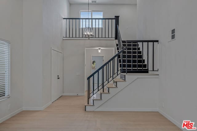 staircase featuring a high ceiling, wood-type flooring, and an inviting chandelier