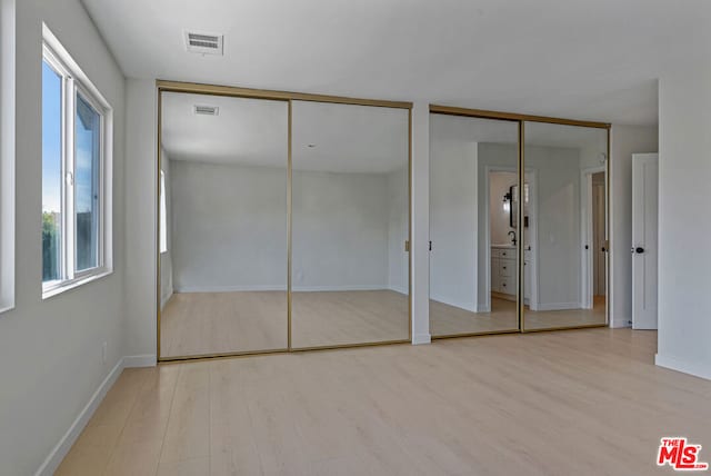 unfurnished bedroom with light wood-type flooring and two closets