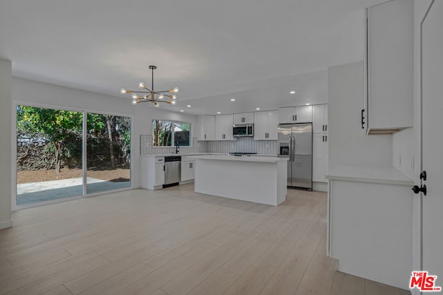 kitchen featuring pendant lighting, appliances with stainless steel finishes, white cabinetry, backsplash, and a chandelier