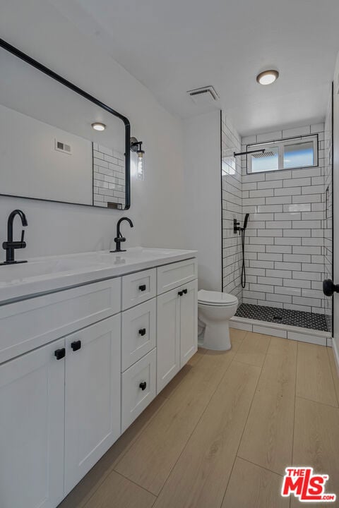 bathroom featuring vanity, wood-type flooring, toilet, and tiled shower