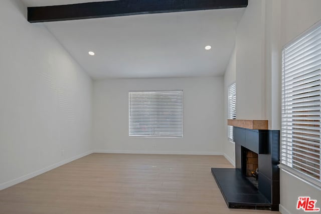 unfurnished living room featuring lofted ceiling with beams, a tile fireplace, and light hardwood / wood-style flooring